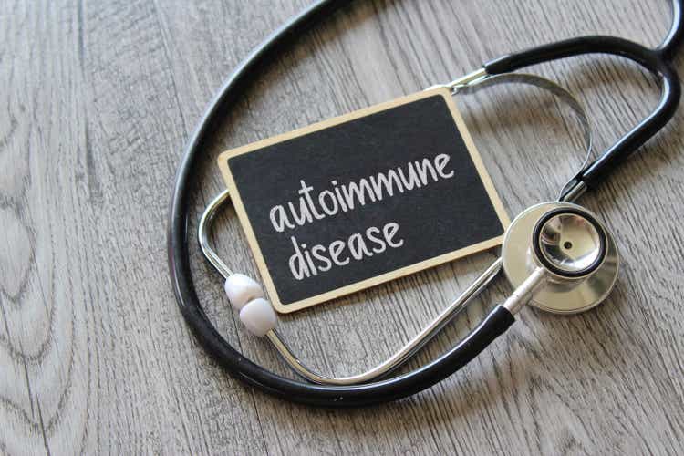 Stethoscope and chalkboard with text AUTOIMMUNE DISEASE on wooden table.