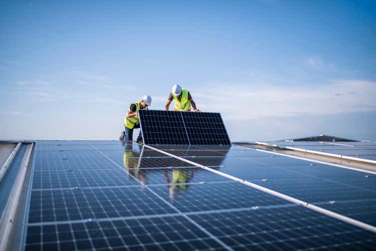 Two engineers installing solar panels on roof.