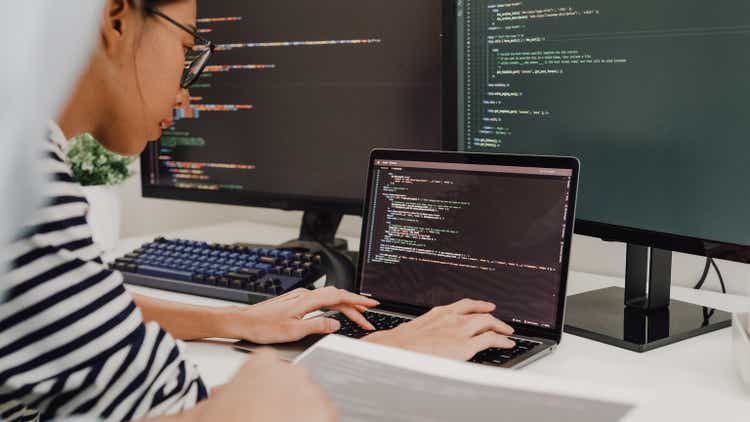 Closeup group of Asian people software developers using computer to write code sitting at desk with multiple screens at office.