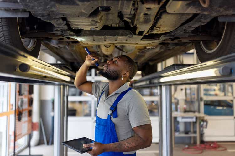 Auto repair specialist examining brake pads of lifted car during inspection