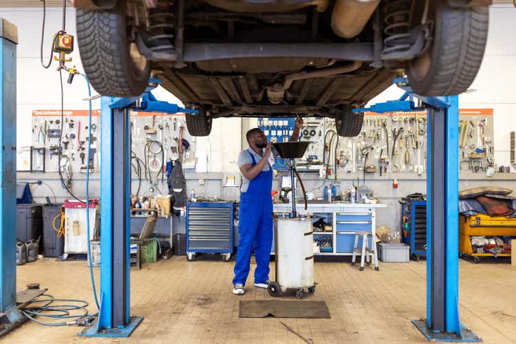 Car mechanic replacing oil from motor engine at garage