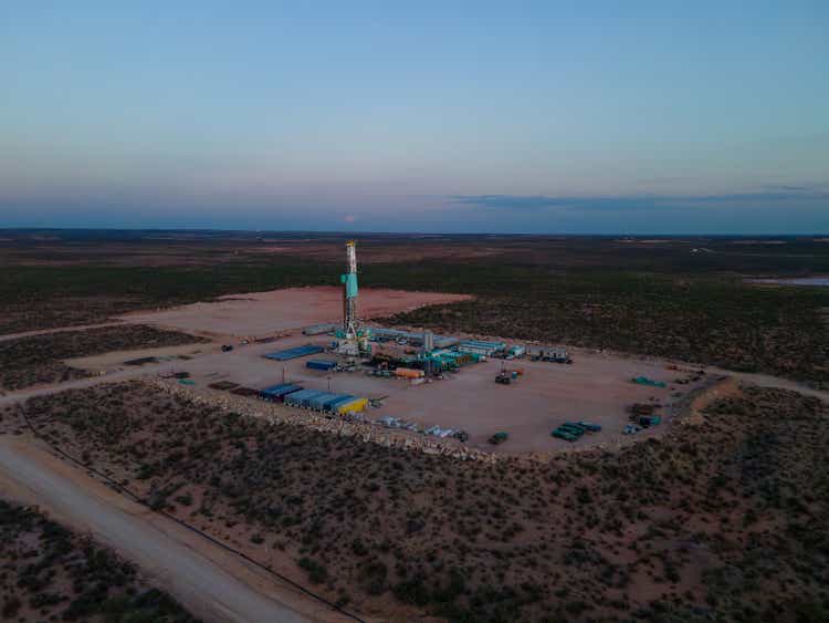 Drone view captures a stunning sunset over the Permian Basin, where a fracking drilling oil rig stands tall, symbolizing the intersection of nature and industry