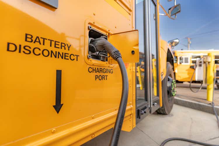 Yellow electric school bus plugged in at a charging station.