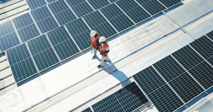 Renewable energy, solar panels and team walking on roof planning for inspection at sustainable business. Engineering, sustainability and photovoltaic power, men in electricity maintenance from above.