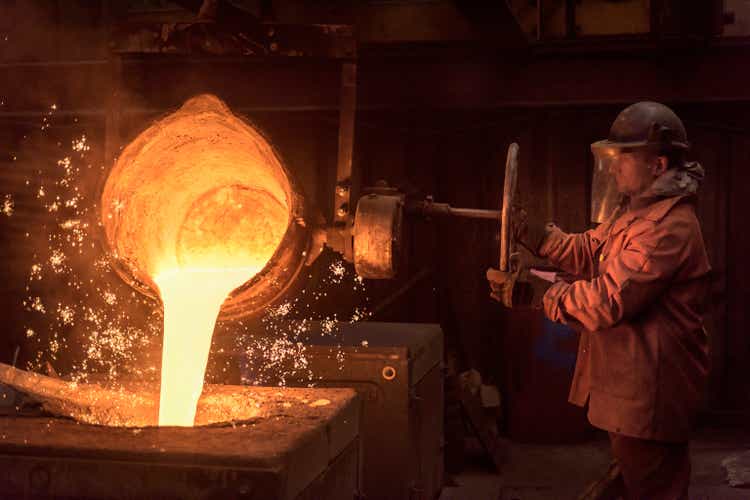 Worker pouring molten metal from flask in foundry workshop