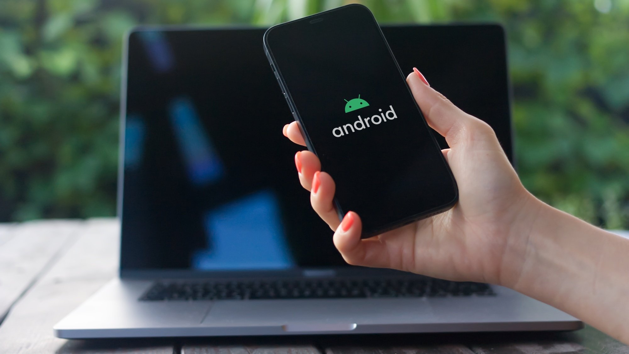 Person holding an Android phone in front of a MacBook