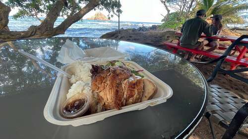 A plate of chicken on a table overlooking Koki Beach. The chicken looks spectacular, grilled to smoky yet moist perfection. It comes with a signature spicy vinegar sauce that's to die for. Sticky rice and a salad with miso dressing is behind it. And oh yeah, there's a pretty beach behind the chicken or whatever.