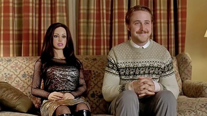 Ryan Gosling as Lars sitting on a couch next to a lifelike doll of a woman in Lars and the Real Girl.