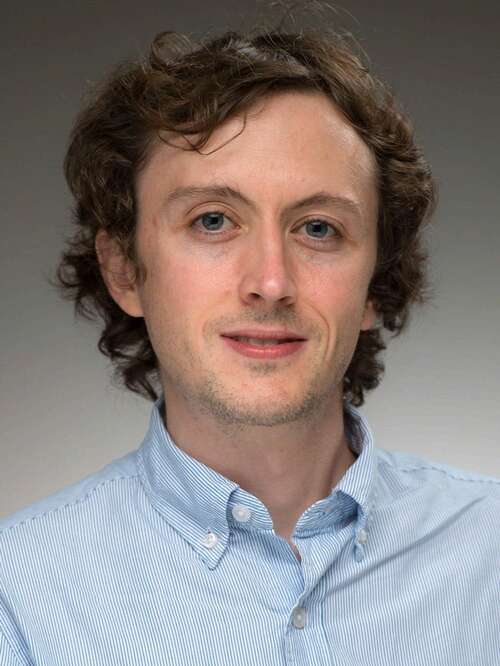 portrait of a man in a blue shirt smiling at the camera against a gray background