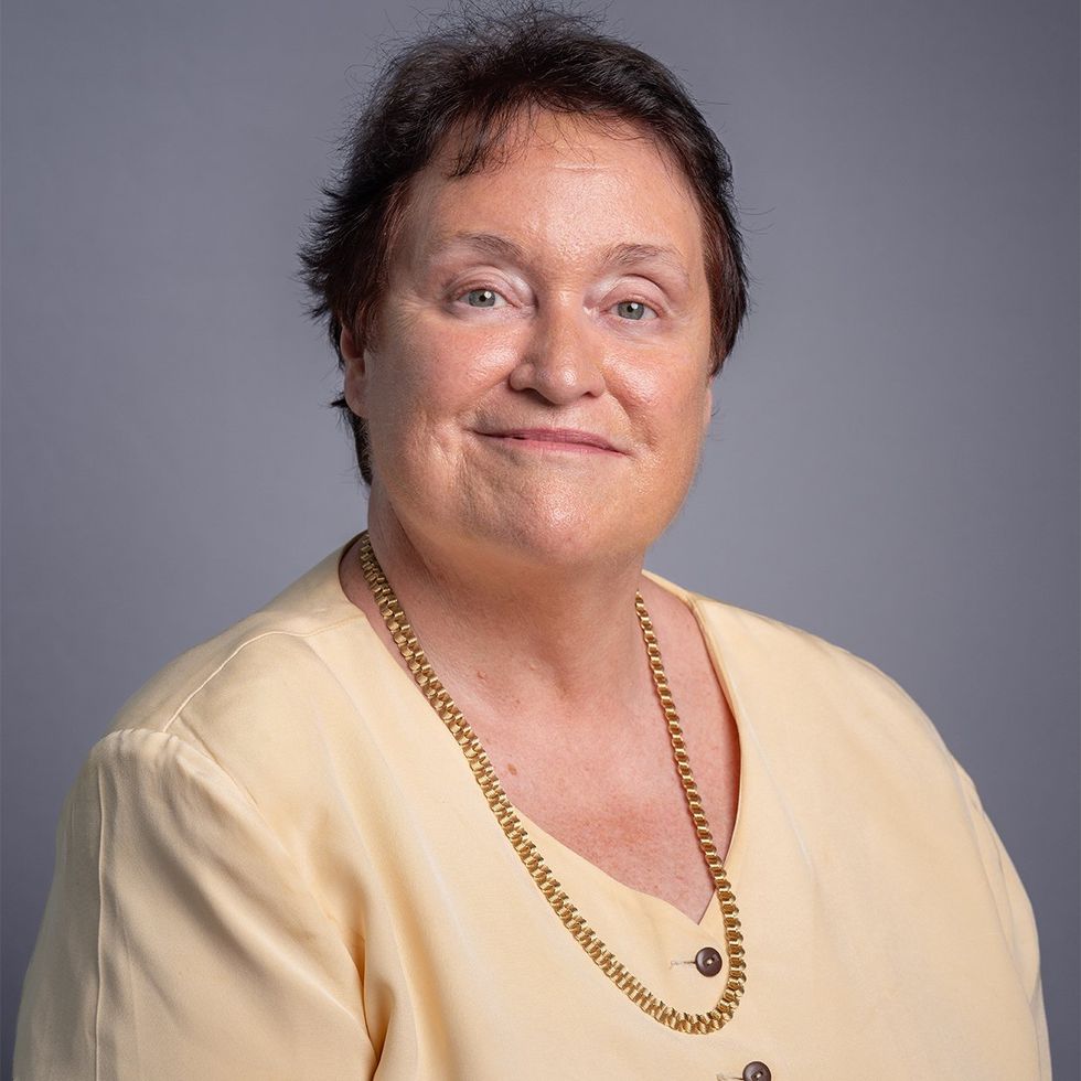 Portrait of a smiling dark haired woman in a yellow shirt and gold necklace.