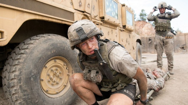 A U.S. solider crouches behind a military vehicle.