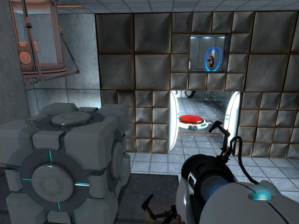 Gameplay still from Valve’s puzzle game Portal. The first-person perspective from atop a platform shows the player holding the portal gun as a cube sits nearby. A red switch lies on the ground in the background behind a door.