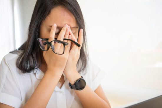 Tired woman holding her glasses between her fingers and rubbing her eyes