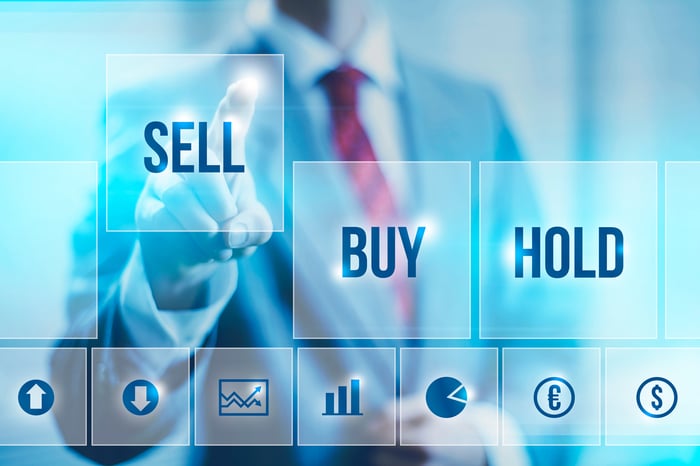 Person in a suit touching a tile with the word Sell next to two tiles that say Buy and Hold.