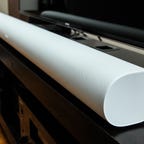 A sideview of a white Sonos Arc soudbar on a black TV stand.