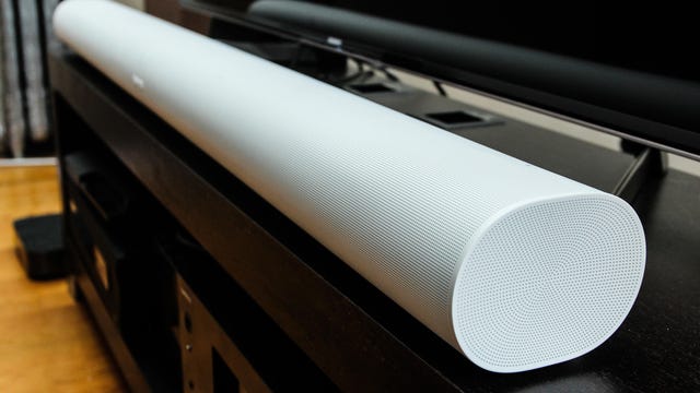 A sideview of a white Sonos Arc soudbar on a black TV stand.