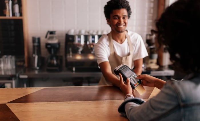 A woman swiping her credit card in the payment machine being held over the counter by a cafe cashier.