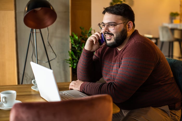 A smiling investor looks at a laptop and talks on the phone.