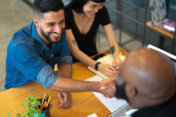 A young couple signing up for a loan and shaking hands with a bank representative.