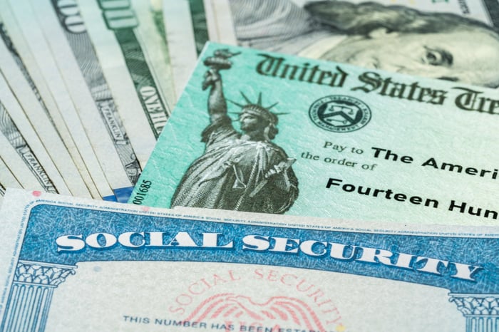 A Social Security card set atop a U.S. Treasury check and U.S. currency.