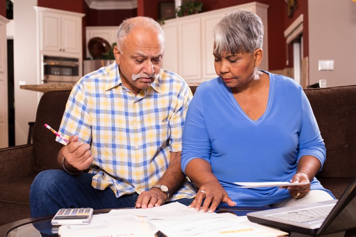 Two people on couch, looking at paperwork on table.