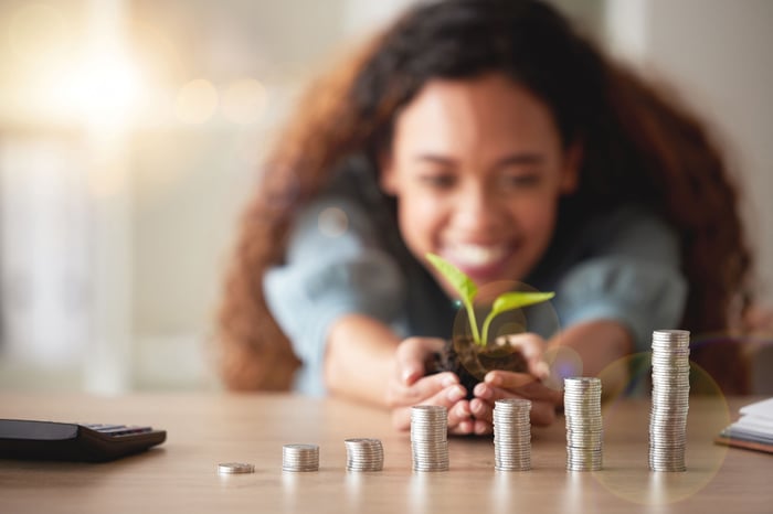 A person holding a seedling and looking at coin stacks.