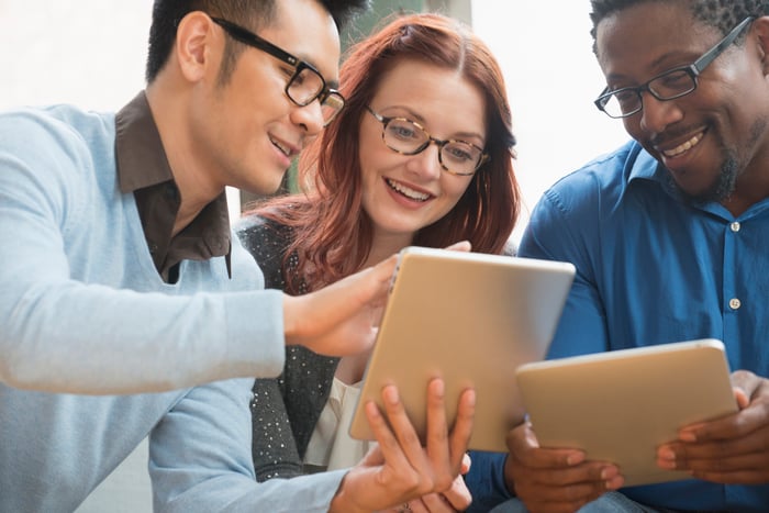 Three investors smile while looking at something on a tablet.