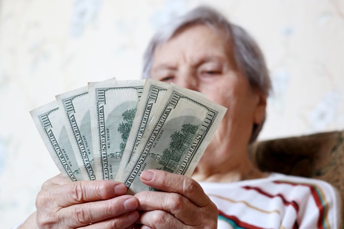 A seated person holding a fanned pile of one hundred dollar bills in their hands. 