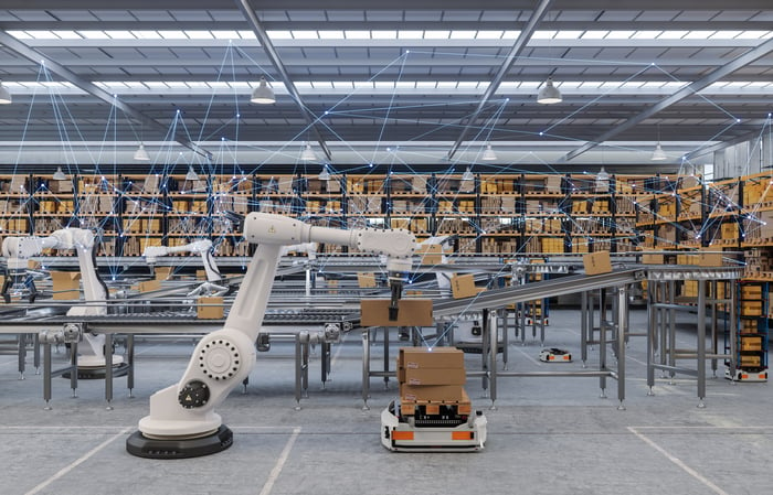 A factory floor with robotic arms sorting packages on shelves and a conveyor belt.