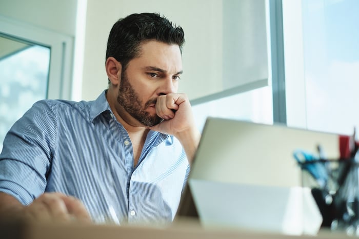 An anxious-looking person pressing their clutched fist against their mouth while looking at a tablet screen. 