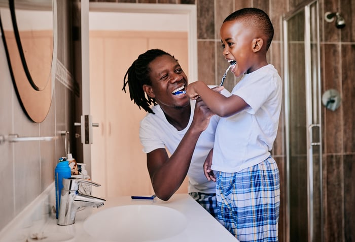 Adult and child brushing their teeth together and smiling.