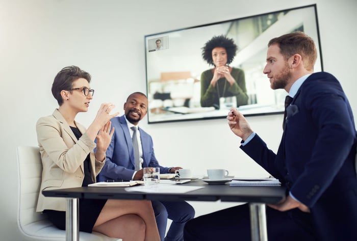 Three employees meet remotely with a fourth employee on Zoom Rooms.