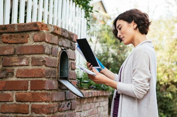 Woman sorting through mail at her mailbox.