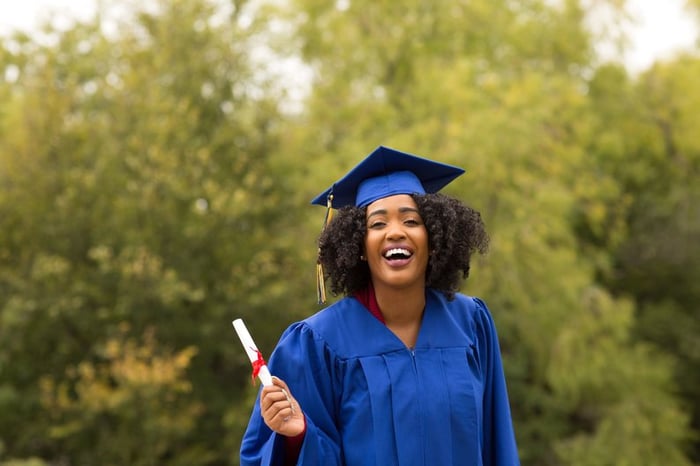 A woman smiling in a college graduation cap and gown.