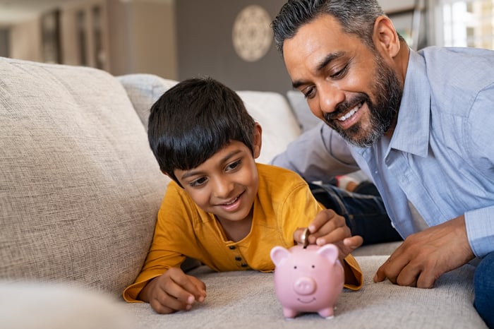 Two people on a couch putting a coin into a piggy bank.