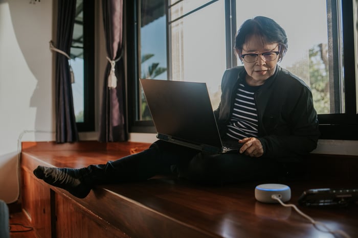 Adult talking on speaker phone and typing on laptop.