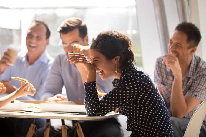 A group of office employees laughing and eating pizza.