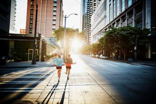 Two people run across the street in an urban area