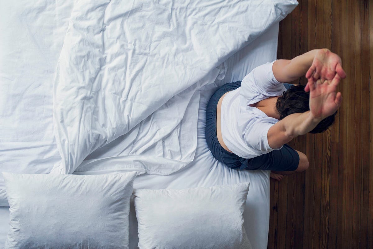 A person sitting on the edge of a bed and stretching