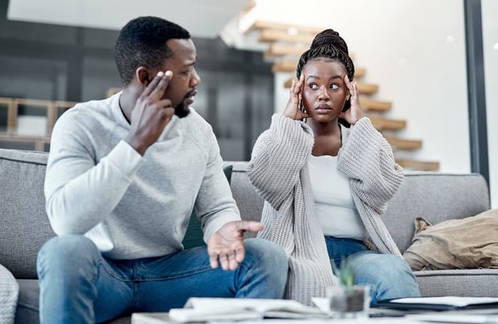 An African /American couple looks at each other worriedly. They sit in front of financial documents and a computer.