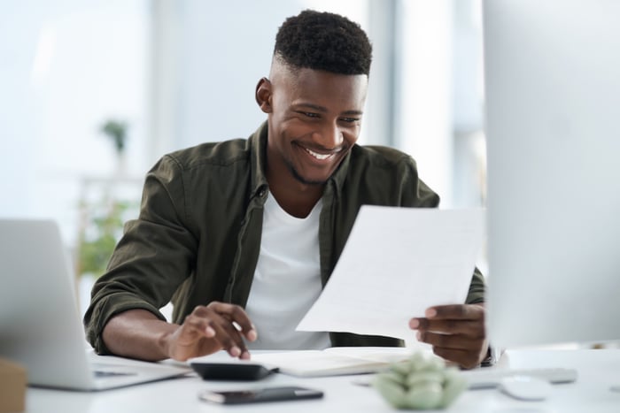 Smiling person looking at paperwork and using calculator. 