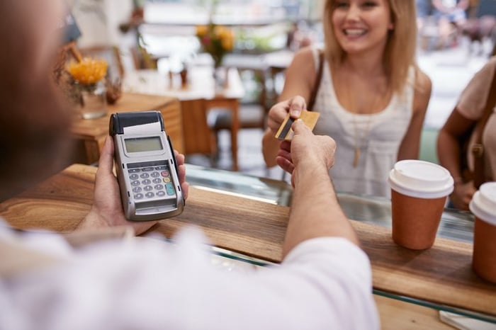 A smiling woman handing her credit card to a coffee shop cashier.