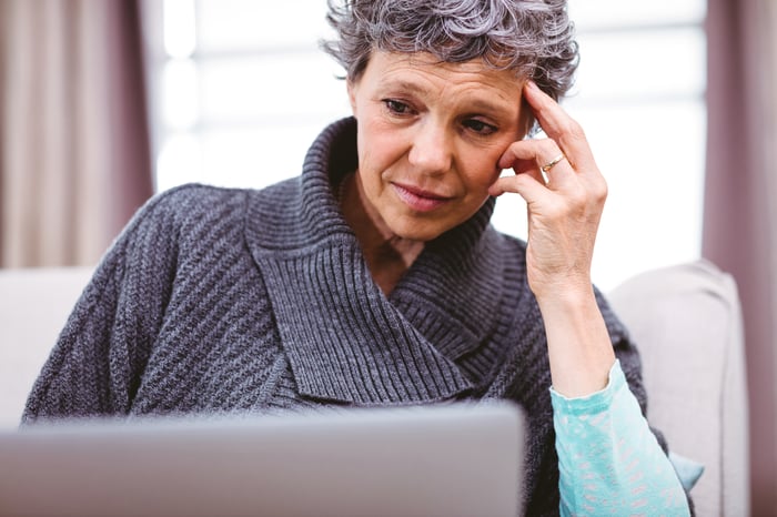 Stressed person with hand on head looking at laptop.