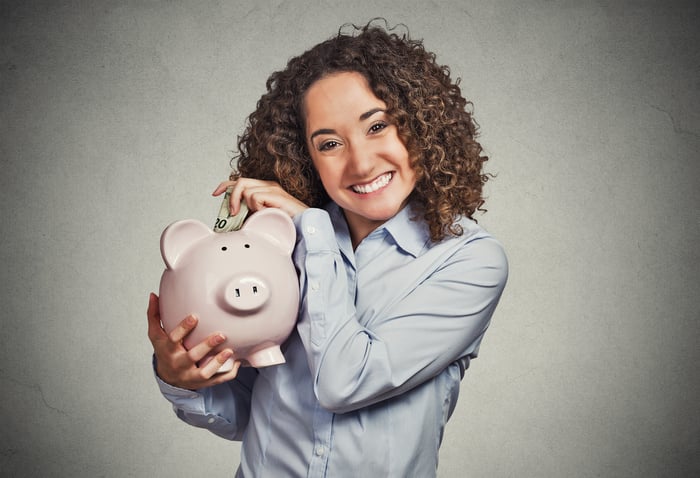 Someone holding a piggy bank while inserting bills into it.