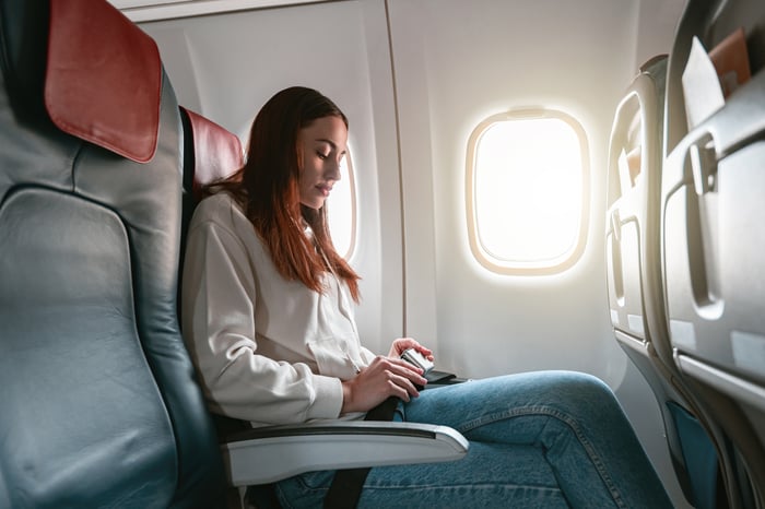 A person on an airplane fastens their seatbelt. 