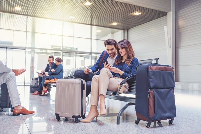 Smiling couple looks at phone together while waiting with luggage in airport