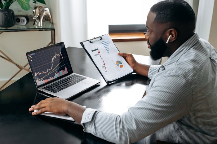 A person reviews a page of financial information and a stock chart on a laptop.