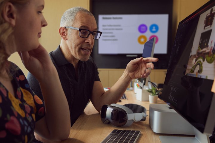 A developer points to a Mac screen while a Vision Pro rests on the desk.