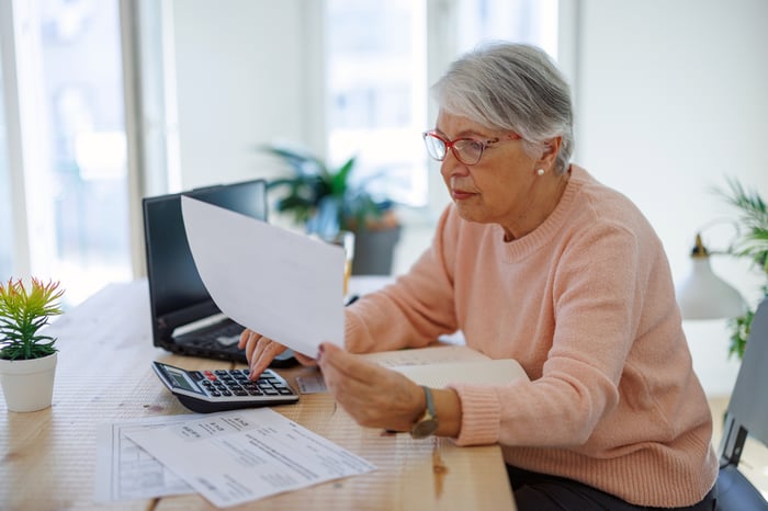 A person at a desk holding a document and using a calculator.