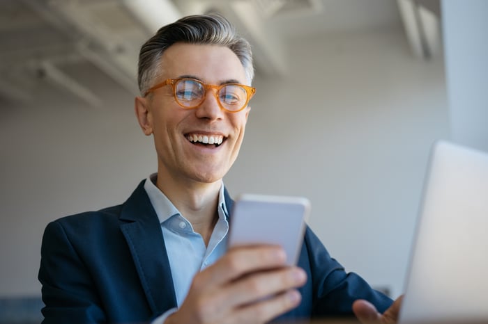 Smiling investor with laptop and smartphone.